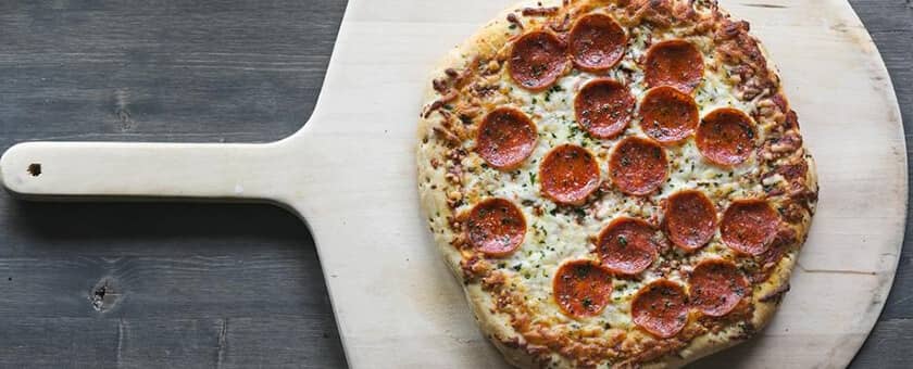 Freshly baked pepperoni pizza on a wooden paddle, symbolizing SysAid’s efficiency in ITSM and Help Desk solutions. - SysAid