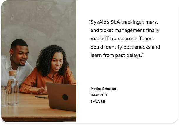 Two colleagues discuss at a table, reviewing SysAid ITSM solutions on a laptop with an IT transparency testimonial displayed. - SysAid