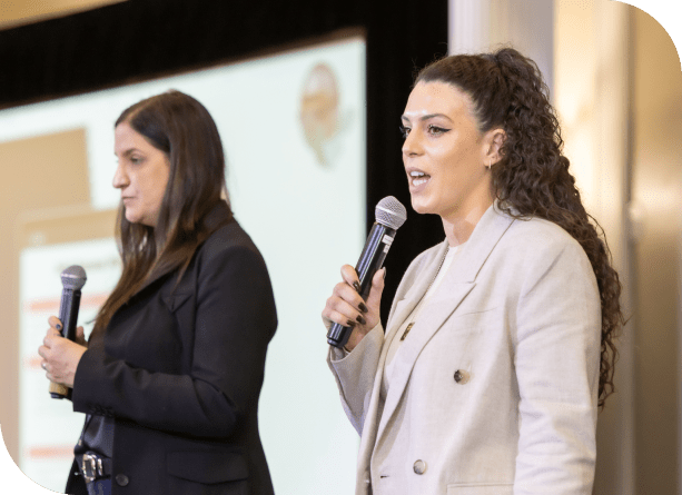Two women lead an ITSM discussion on stage at a SysAid event, sharing insights with the audience. - SysAid