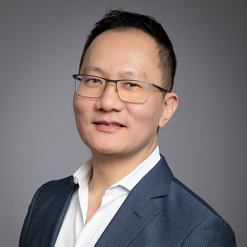 Professional headshot of a middle-aged asian man wearing glasses, a blue blazer, and a white shirt, smiling slightly at the camera.