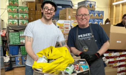 Two men smiling in a food pantry, symbolizing SysAid Service Desk support delivering ITSM solutions for teamwork. - SysAid
