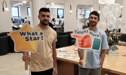 Two colleagues celebrate ITSM success at SysAid office event, with teamwork recognized in a service desk environment. - SysAid