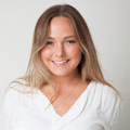 A smiling young woman with long, blonde hair in a white top, posing against a light gray background.