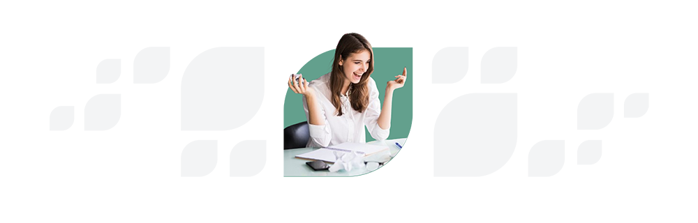 A woman with brown hair gesturing excitedly at a laptop screen while sitting at a desk with papers.